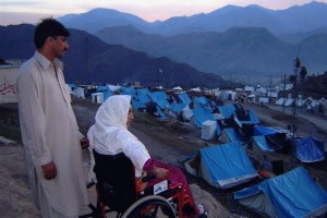 Image of a refugee camp showing a man and a woman in a wheelchair looking at the camp in the sunset