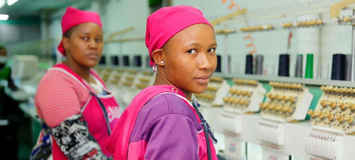 © ILO/Marcel Crozet Garment workers stand next to a line of sewing machines in a clothing plant in Lesotho.