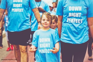 A young girl with Down's Syndrome walks with two others, with T-shirts reading Down Right Perfect
