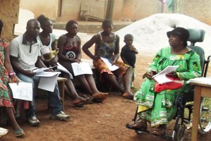 Image of woman in wheelchair presenting to group in a village setting