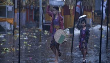 © ESCAP/Armin Hari A mother and her daughter try to shield themselves from rain as they walk in a market.