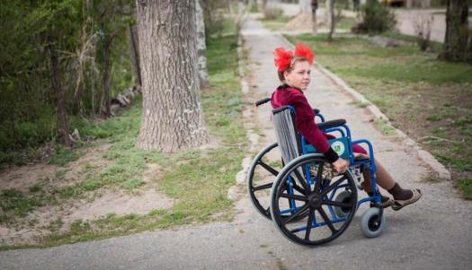 © UNICEF/Gabriel Vockel A young girl in a wheelchair moves along a path in Kyrgyzstan.